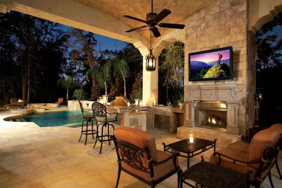 A well-lit patio and pool area with a Seura outdoor TV above a fireplace.